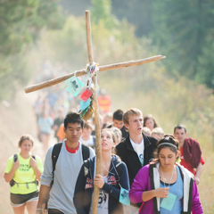 Students carry a wood cross as they walk on a trail in the forest