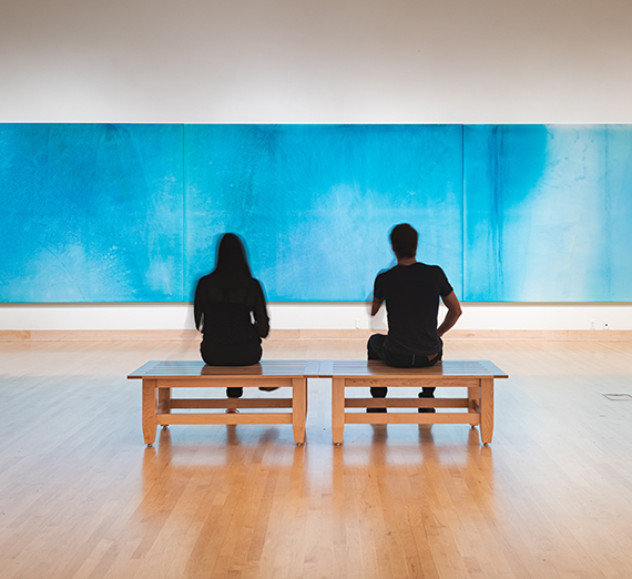 Two people sit in front of a large blue painting.