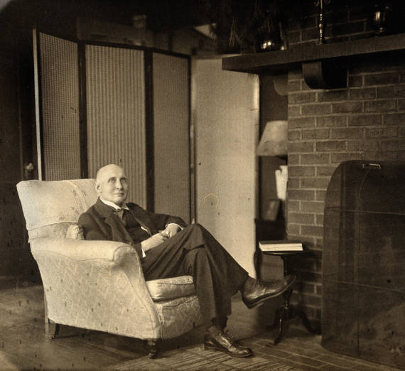 Alfred Whitehead seated in front of fireplace. 