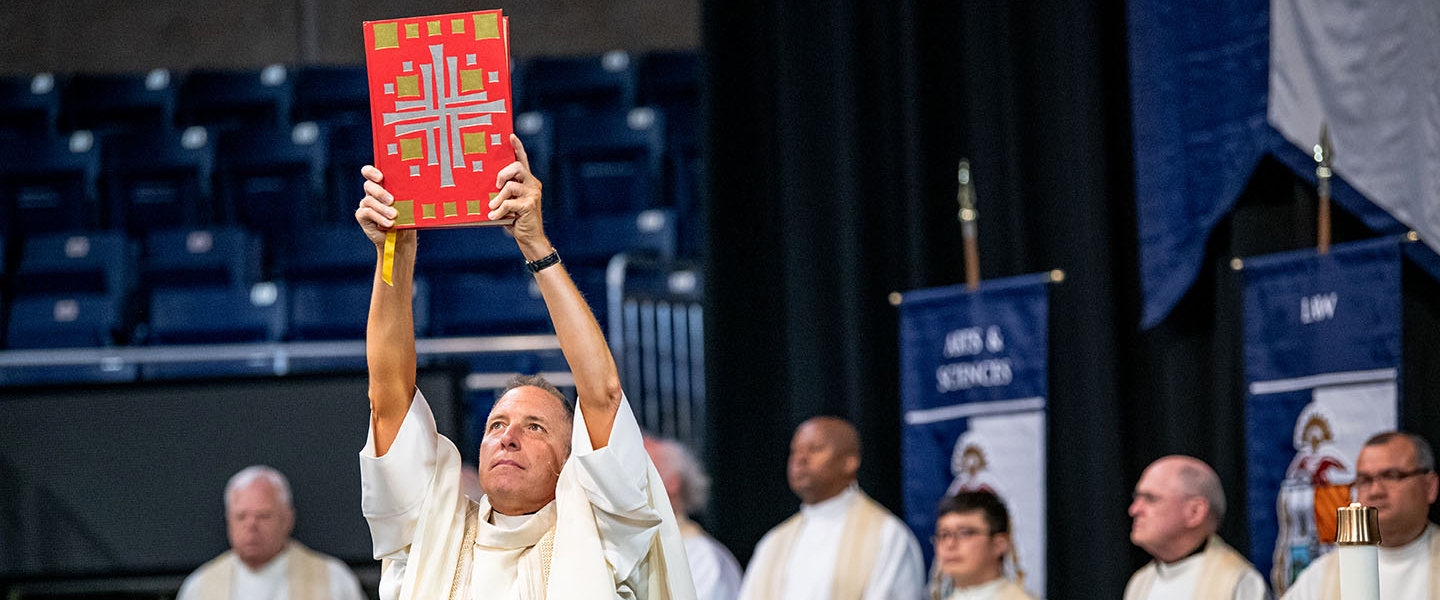 Fr. Hess holding up the book of the gospels at commencement mass