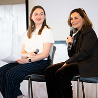 Two individuals sit on chairs holding microphones.