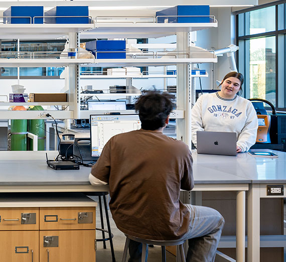 Two students talk at computer stations in a clean lab