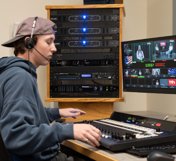 Student operating a professional video switcher and broadcast control system at Gonzaga University, managing live production feeds on dual monitors for the Broadcast Journalism Minor program.