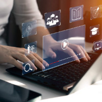 A laptop computer with hands on it and icon images in the air above the keyboard.