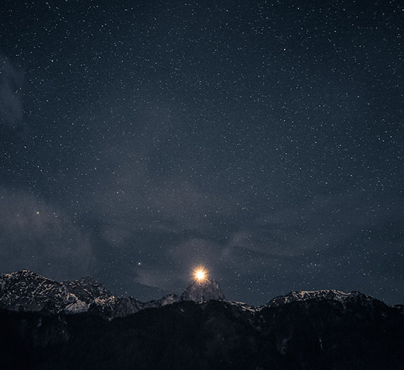 Image of a starry, moonlit night over a mountain range