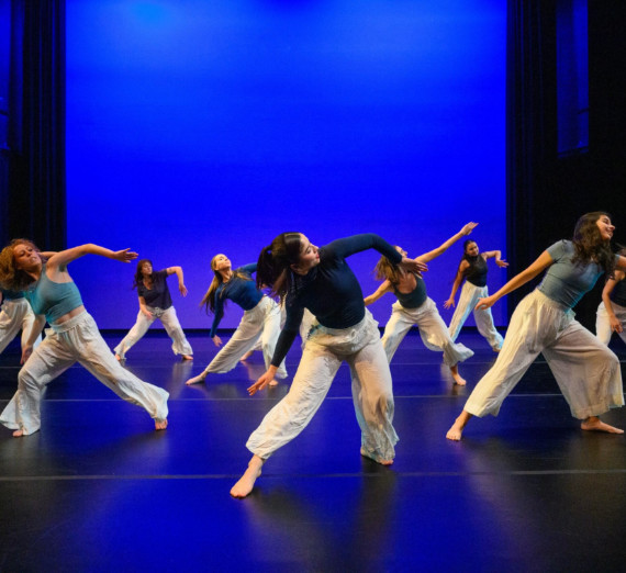 A group dancing in unison in front of a blue background.