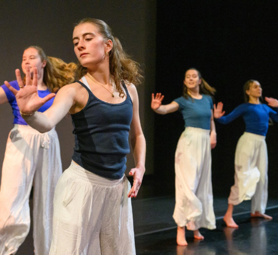 A group dancing in unison against a black background. 