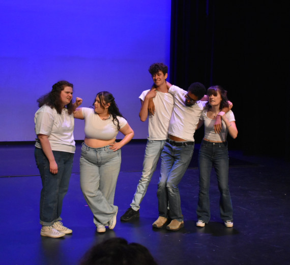 Four students in white shirts and jeans performing a scene.