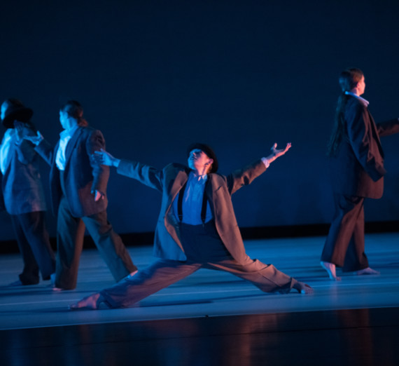 Dancing students in suits, center stage is going into splits.
