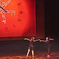 Two dancers in front of large clock image.