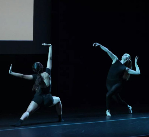 Two dancers on dark stage dancing dramatically.