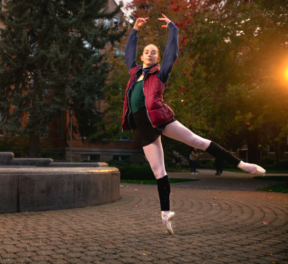 Student performing a ballet move in front of College Hall while wearing a vest. 