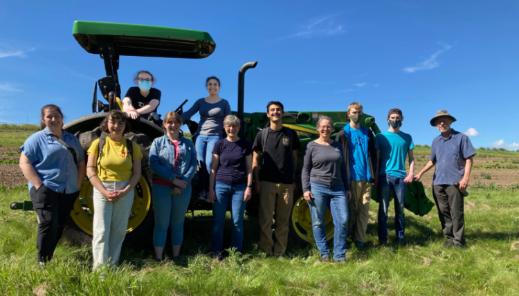 Students and faculty grouped with a tractor in a field. 