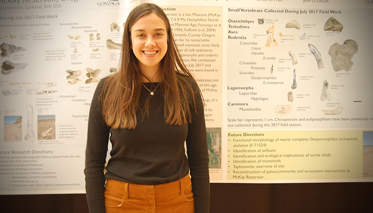 A student proudly stands in front of her research project board.
