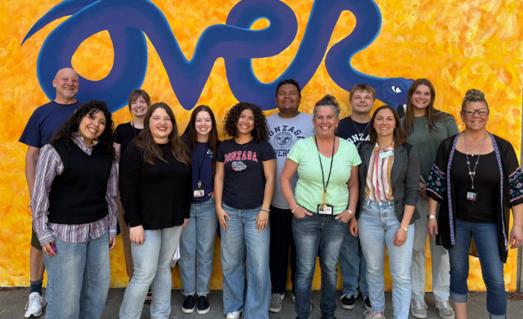 A group of students posed in front of a bright yellow wall.