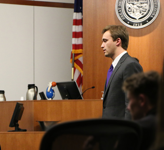Luke Pfister stands in front of a mock trial court room.