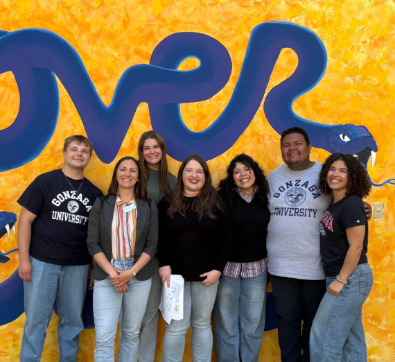 A group of students posed in front of a bright yellow wall. 