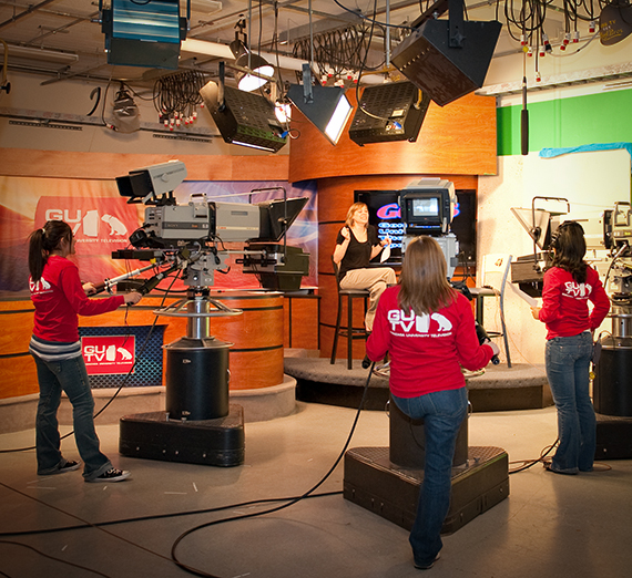Broadcast journalism students recording video in a news studio setting.
