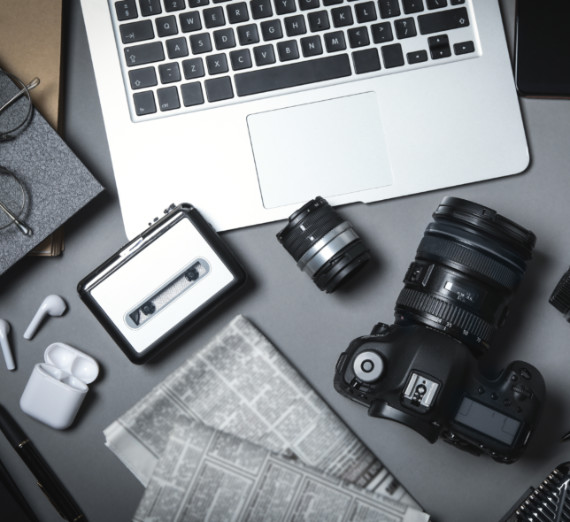 Stock image of journalism supplies including a computer, cassette player, camera, newspaper, and headphones.