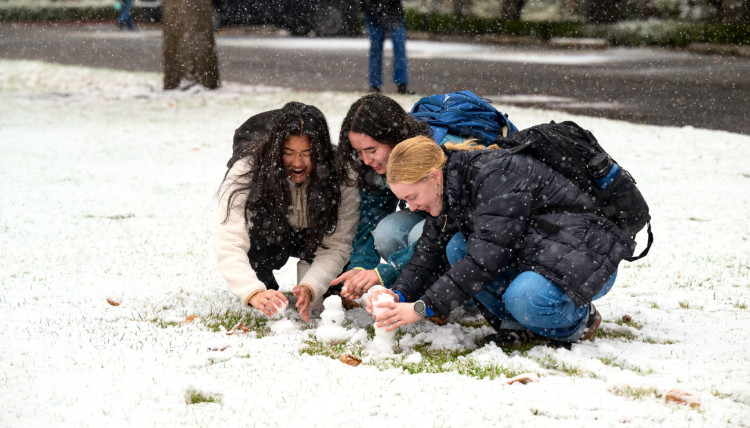 Three Gonzaga University students building tiny snowmen with the small amount of snow that has fallen.