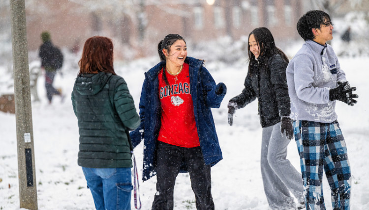 Four students laughing and playing in the snow on campus on a snowy day.