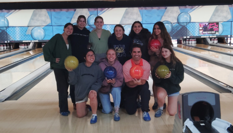 The Social Interdependence Lab student workers and Dr. Adam Stivers posed with bowling balls in front of the bowling lanes.