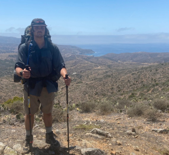 Declan Gallup with a backpack and hiking poles in an arid environment. 