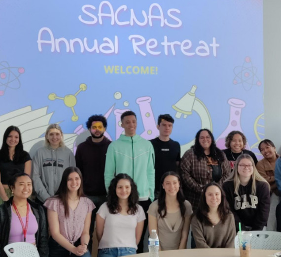 Students from the Society for the Advancement of Chicanos/Hispanics and Native Americans in Science standing in front of a screen that says "SACNAS Annual Retreat".