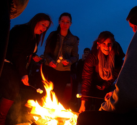 Students gathered around a campfire roasting marshmallows.