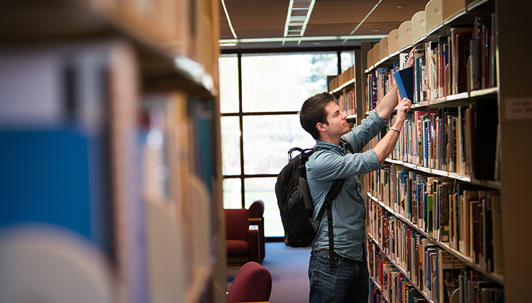 A student pulling a book off of a shelf in Foley Library
