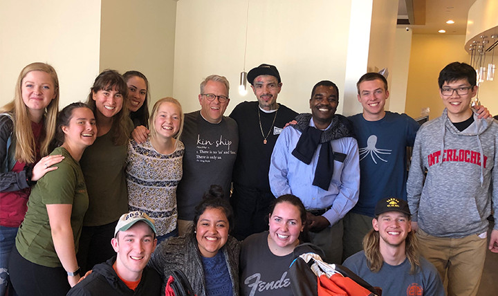 A group of men and women - students, a professor, a priest, and an employee at Homegirl Café - smile for a photo at Homeboy Industries