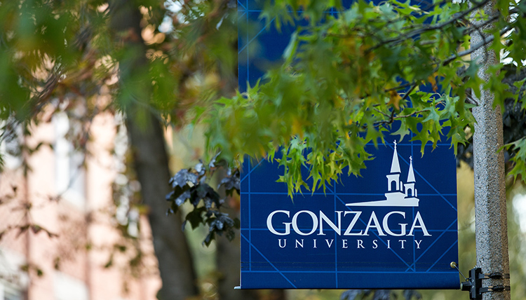A blue Gonzaga post banner behind green tree leaves