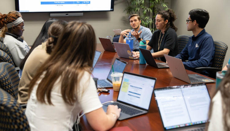 Students and faculty from the School Psychology department sit around a table with their laptops open