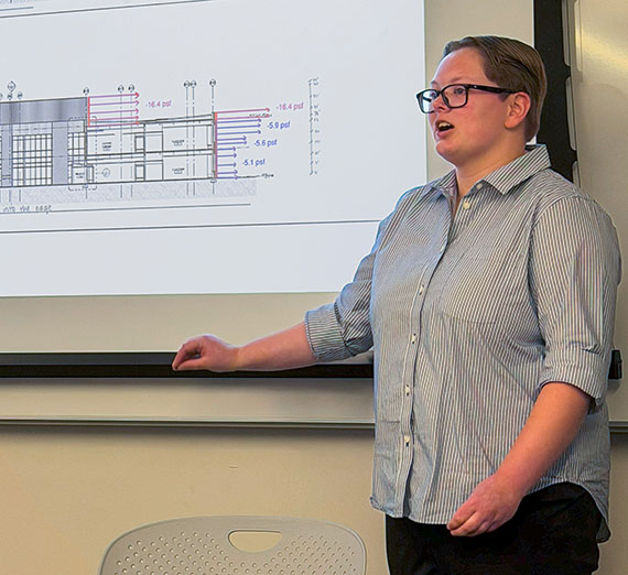 A young woman gestures to a diagram shown on a projection screen