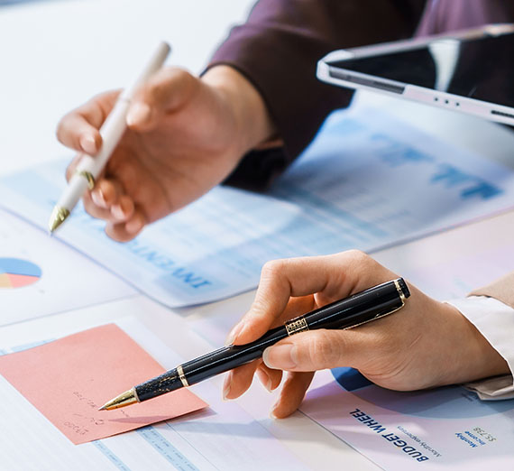 Two hands each holding a pen on a table of papers