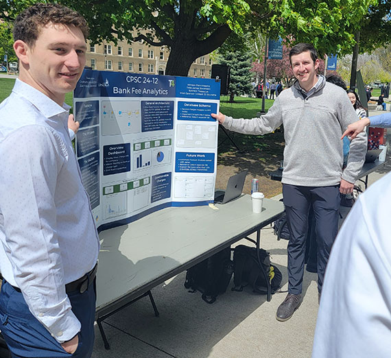 two engineering students stand next to their academic poster