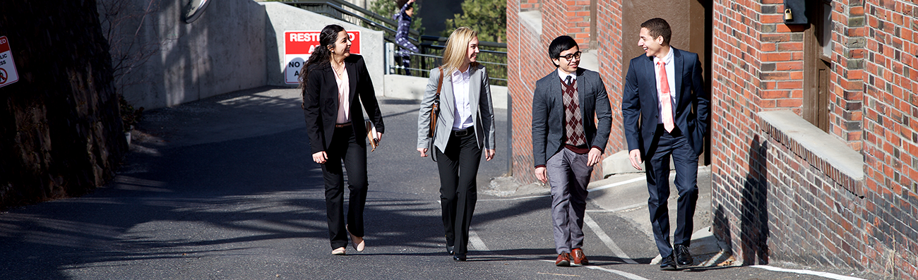 Four students dressed professionally walking on a street next to one another.