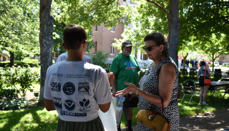 A Climate Institute staff member faces away from the camera while talking to a community member during the urban heat island mapping campaign. On the back of her shirt are the logos of the partners that made the project possible