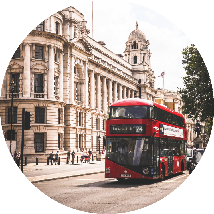 A red double-decker bus drives past the front of a long, white columned building in downtown London.