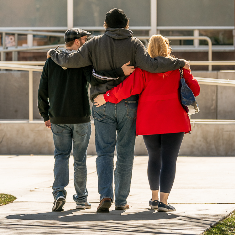 A trio walk towards Crosby with their arms around each other and their backs facing the camera.