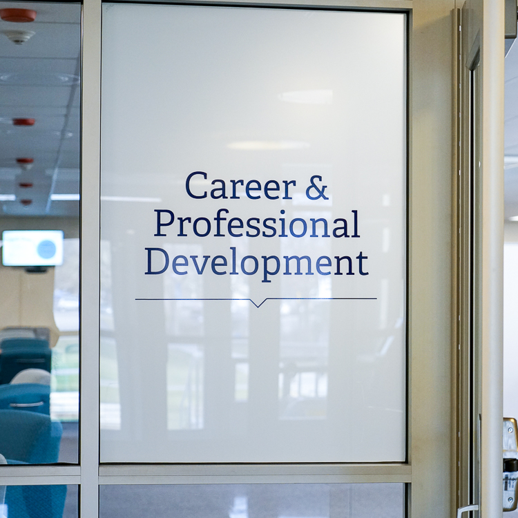 Image of the glass front doors of the Crosby lobby. A frosted panel to the left of the door has blue text printed on it that reads "Career & Professional Development."