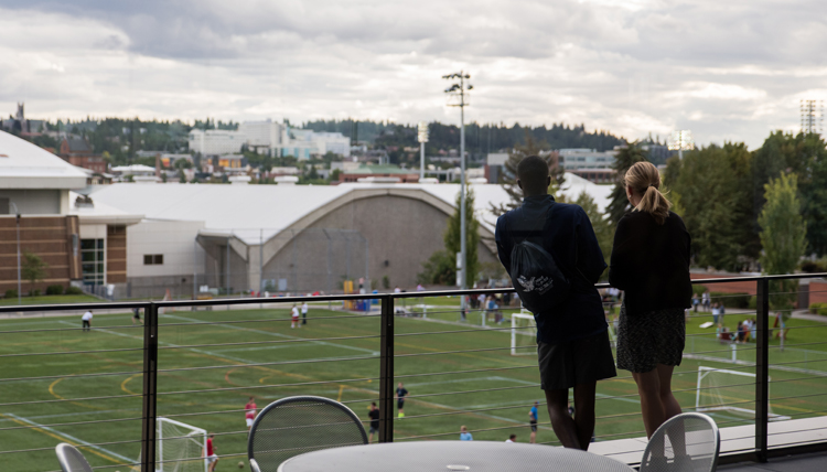 Two GU students stand on Hemmingson balcony overlooking mulligan turf field