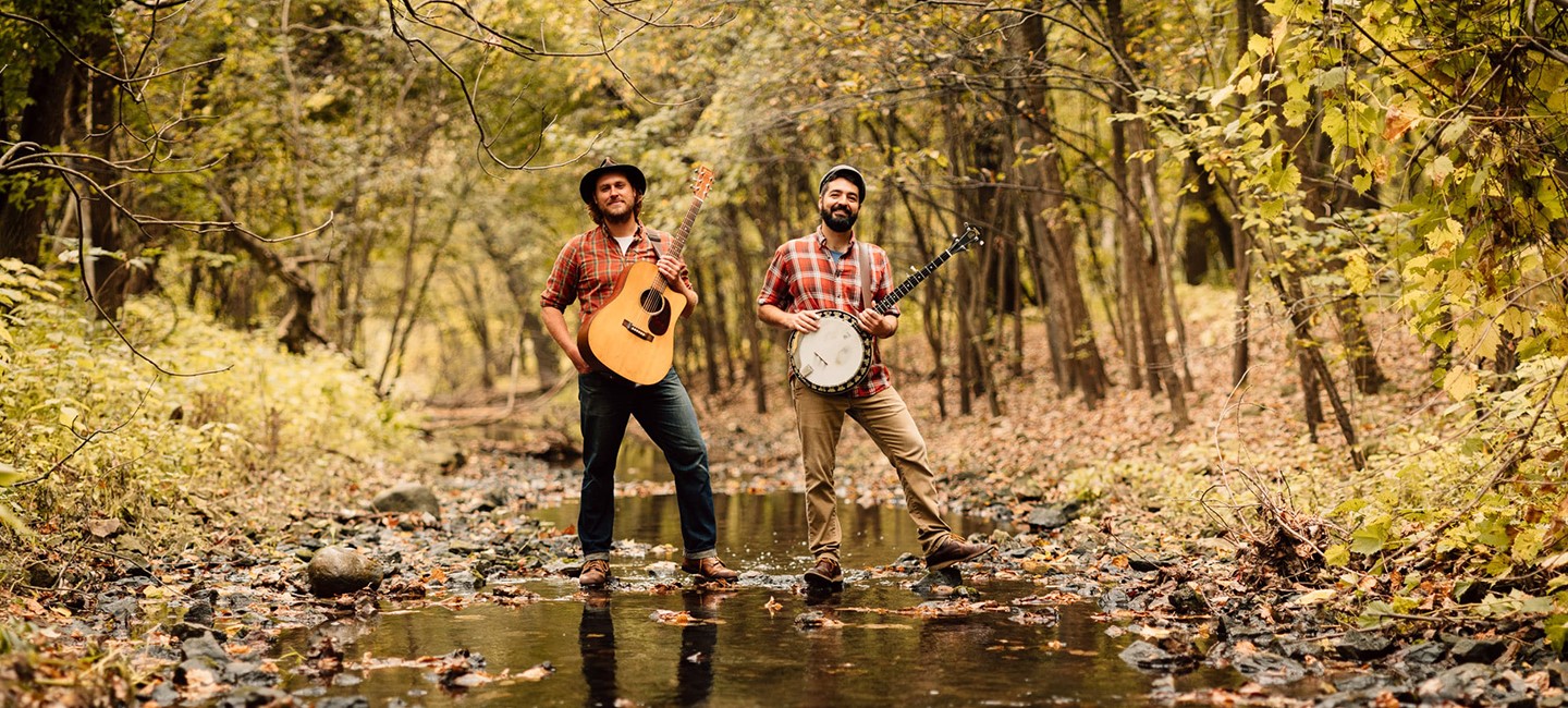 Members of Okee Dokee in a forest with their instruments.