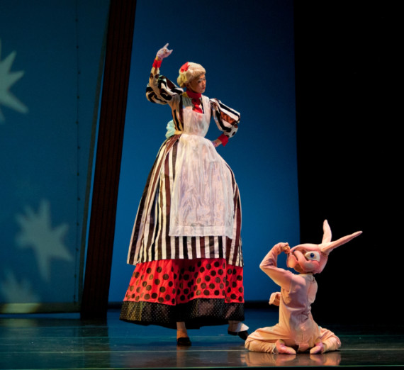 A scene from the stage performance of The Velveteen Rabbit where the rabbit is kneeling on the floor in front of a very tall person in a dress, cap and apron.