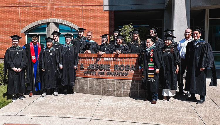 Graduates from Master's in Sport and Athletic Administration standing in front of the School of Education in their caps and gowns.