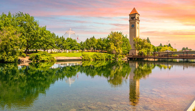 The Spokane Riverfront Park clocktower with a brilliant orange and blue background sky reflecting off the river.