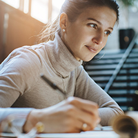 A woman looking at a laptop screen and writing