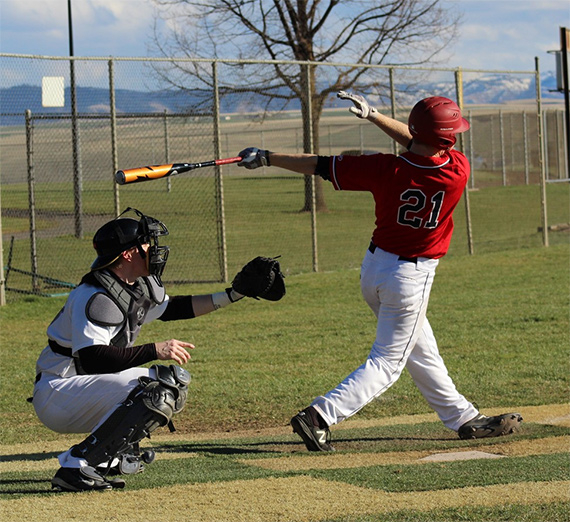 A batter takes a powerful swing at a baseball while the catcher crouches behind him