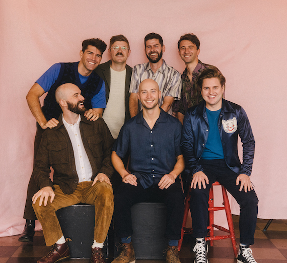 photo of seven men in front of a pink backdrop