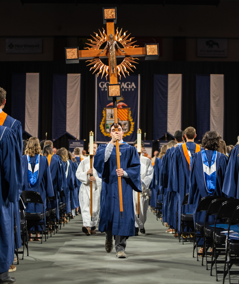 Student in commencement attire carries a cross